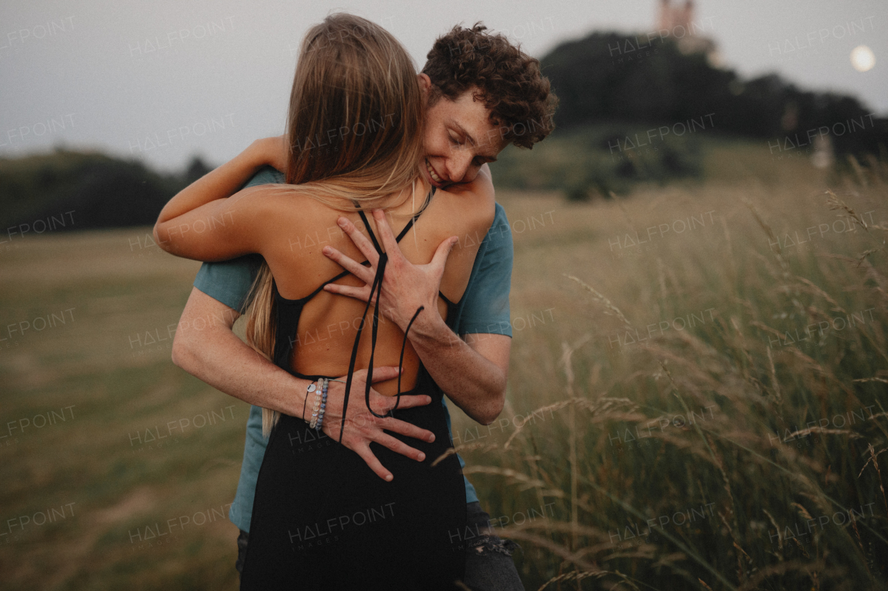 Side view of young couple on a walk in nature at sunset in countryside, hugging.