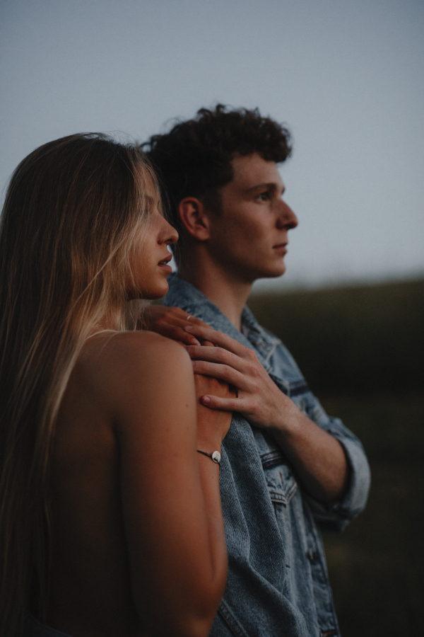 Side view of young couple on a walk in nature at sunset in countryside, standing.