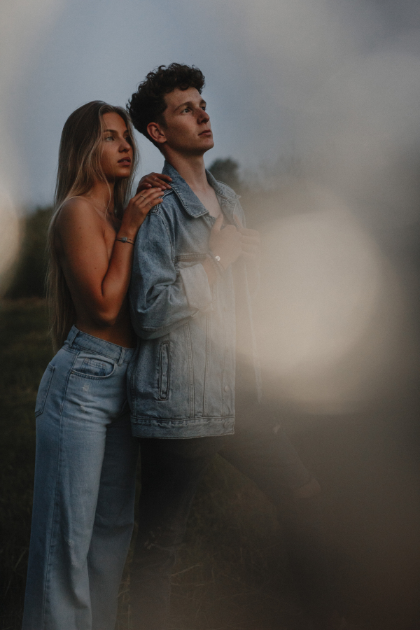 Side view of young couple on a walk in nature at sunset in countryside, standing.