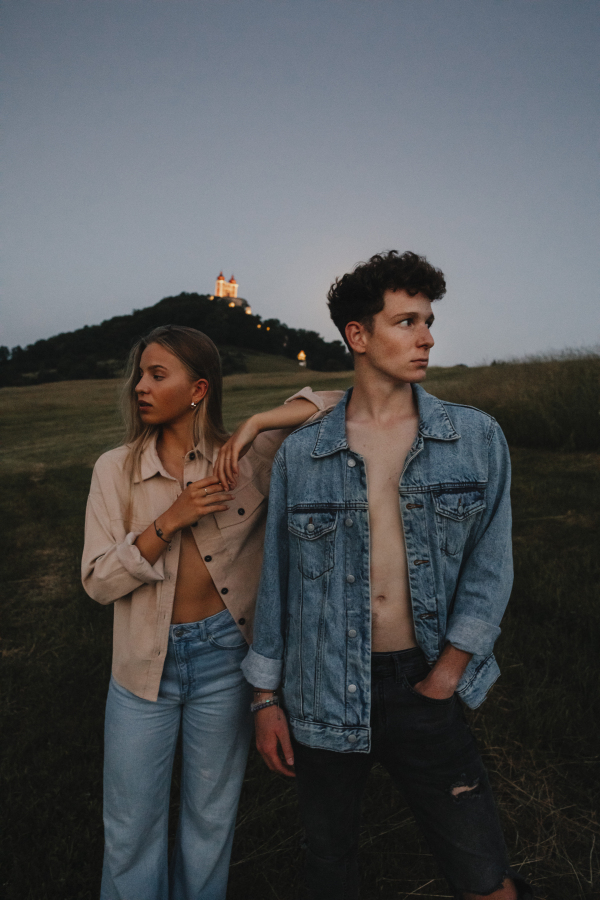 A portrait of young couple standing in nature in countryside, looking away from each other.