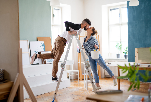 Happy mid adults couple kissing when painting indoors at home, relocation and diy concept.