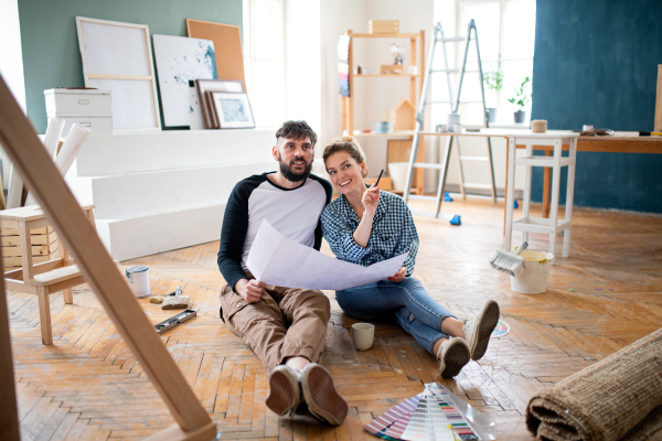 Front view of mid adults couple with blueprints planning indoors at home, relocation and diy concept.