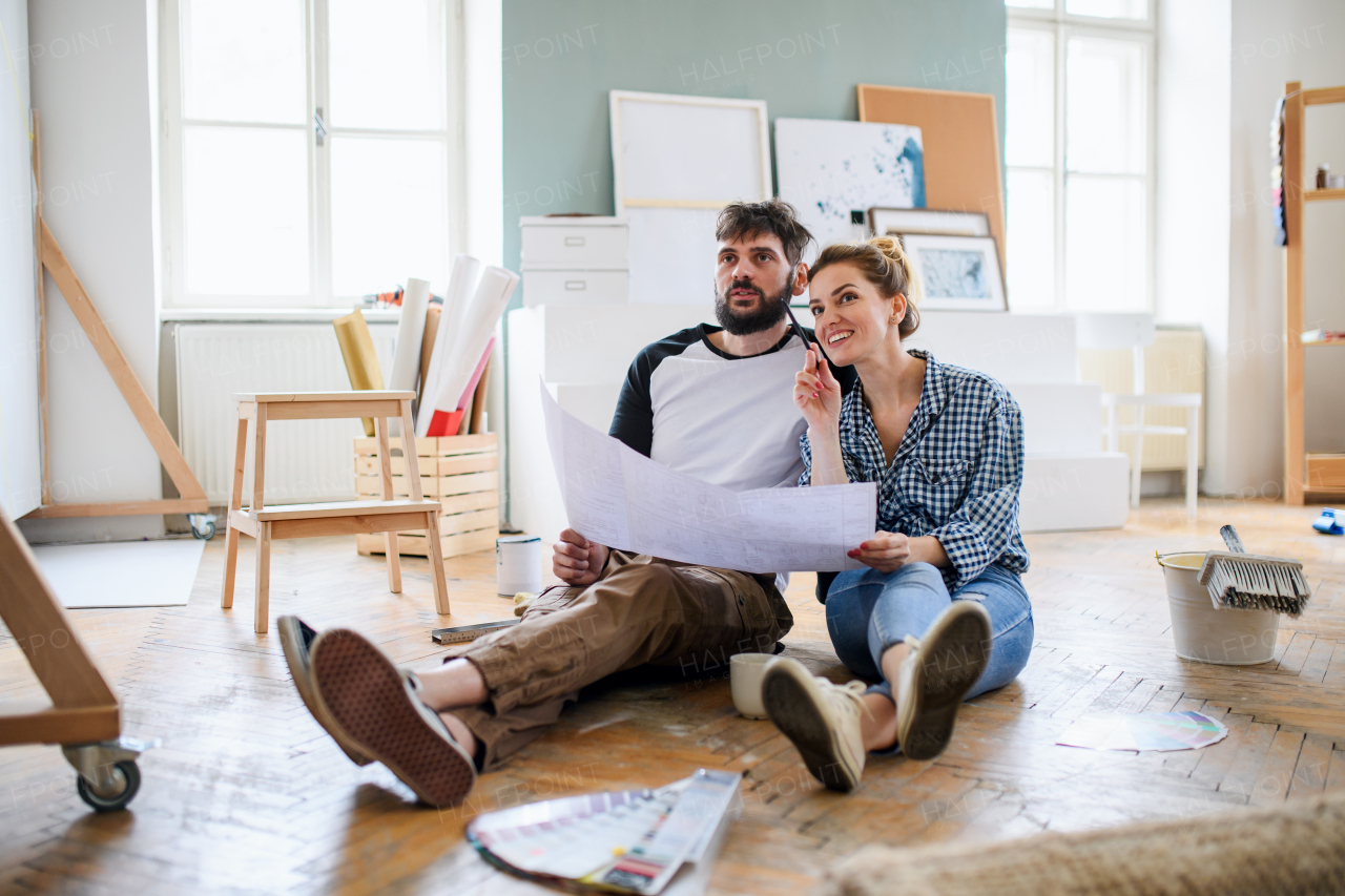 Front view of mid adults couple with blueprints planning indoors at home, relocation and diy concept.