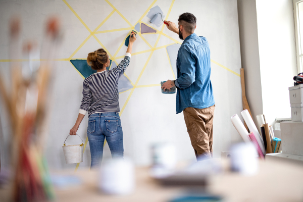 Rear view of mid adults couple painting wall indoors at home, relocation and diy concept.