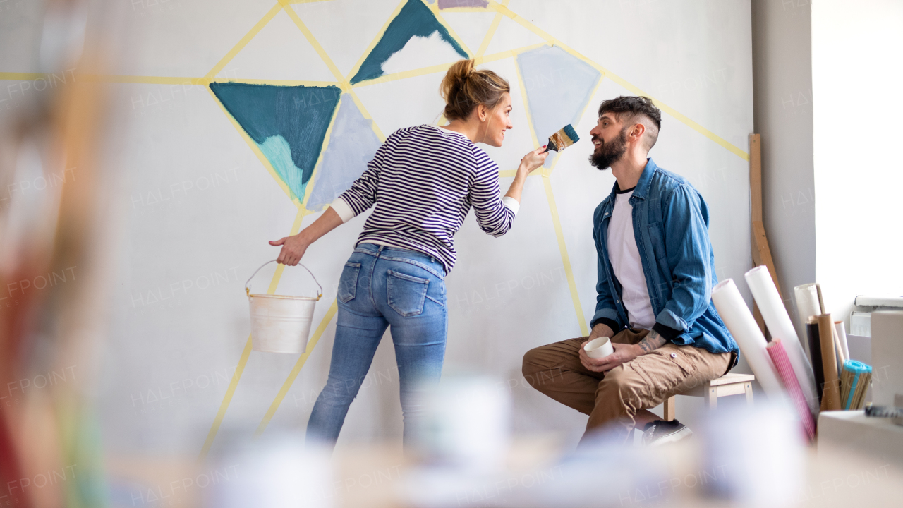 Mid adults couple having fun when painting wall indoors at home, relocation and diy concept.