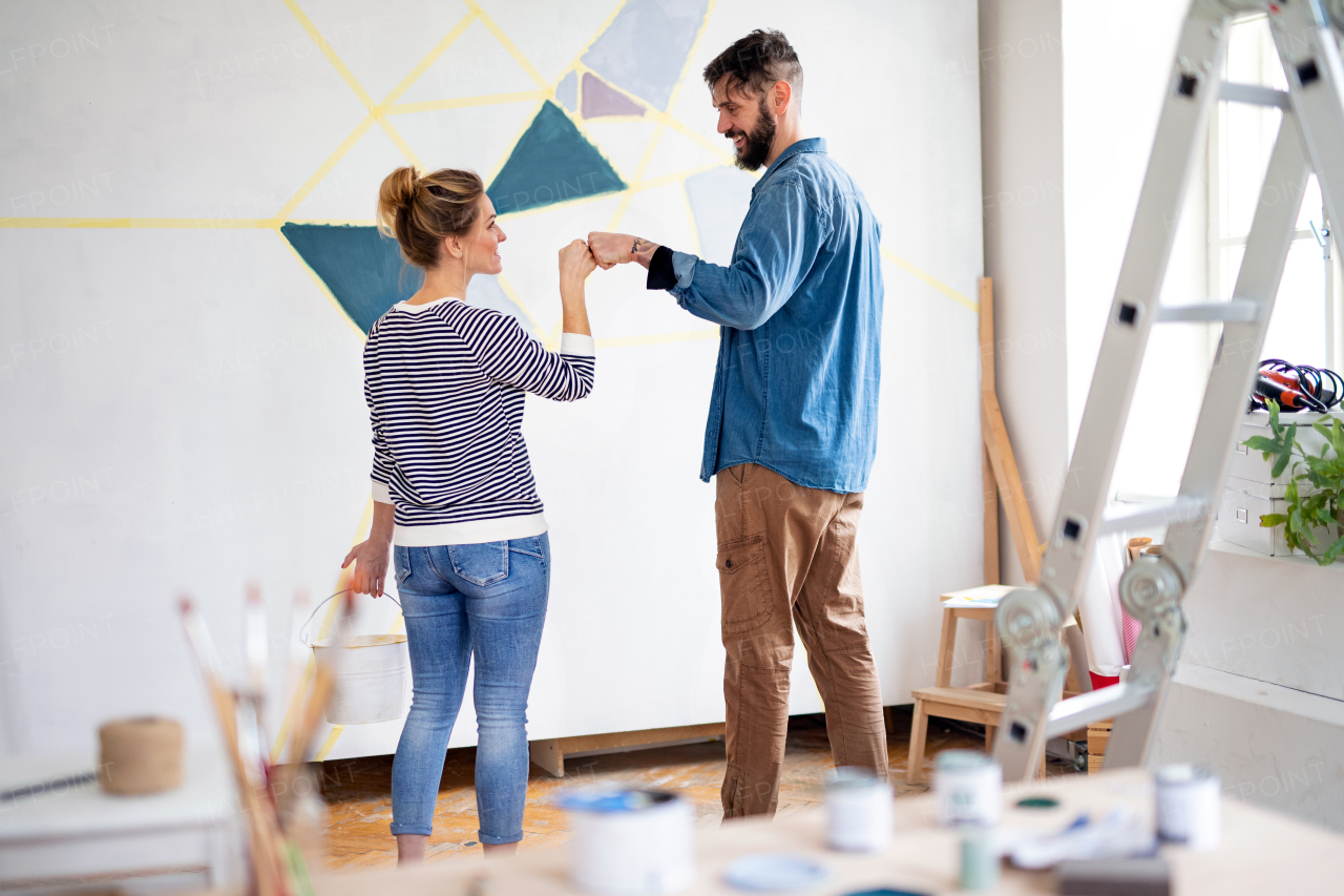 Mid adults couple having fun when painting wall indoors at home, relocation and diy concept.