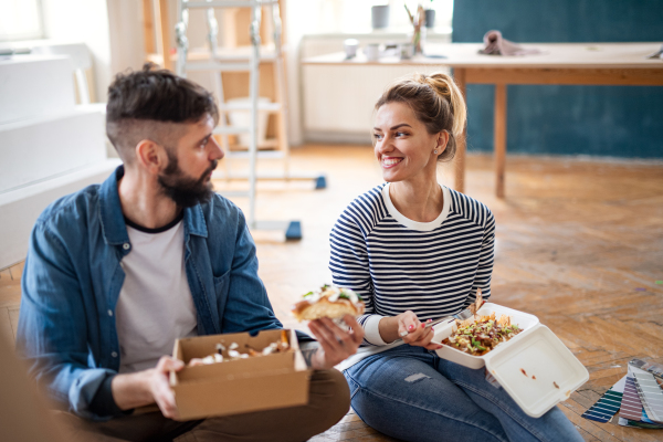 Mid adults couple eating lunch indoors at home, relocation, diy and food delivery concept.