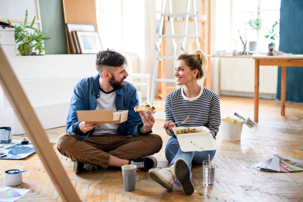 Mid adults couple eating lunch indoors at home, relocation, diy and food delivery concept.