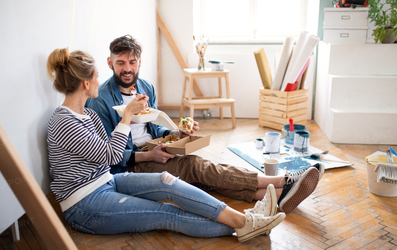 Mid adults couple eating lunch indoors at home, relocation, diy and food delivery concept.