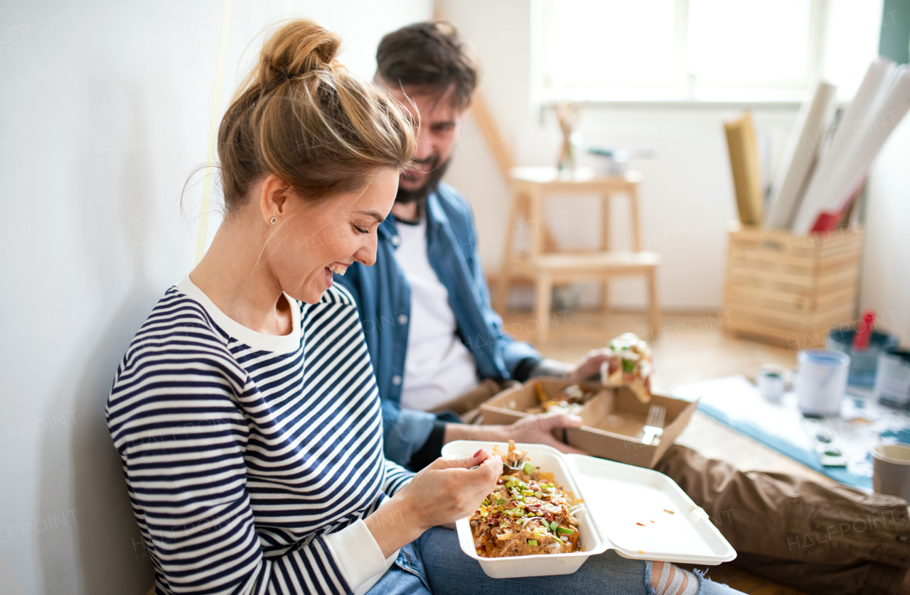 Mid adults couple eating lunch indoors at home, relocation, diy and food delivery concept.