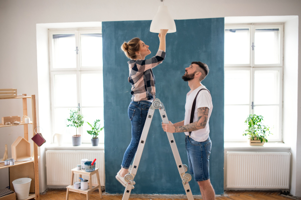 Happy mid adults couple changing light bulb indoors at home, relocation and diy concept.