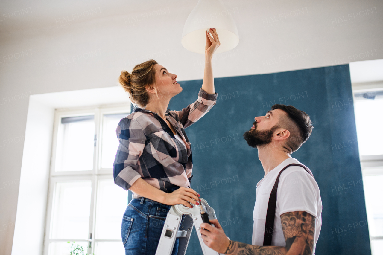 Happy mid adults couple changing light bulb indoors at home, relocation and diy concept.