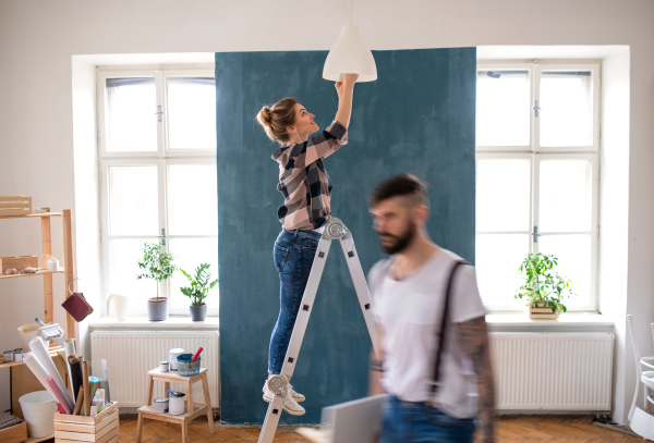 Happy mid adults couple changing light bulb indoors at home, relocation and diy concept.