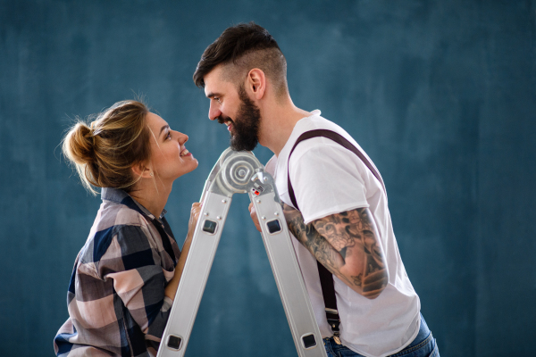 Happy mid adults couple on ladder indoors at home, relocation and diy concept.