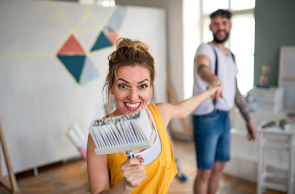 Mid adults couple having fun when painting wall indoors at home, relocation and diy concept.