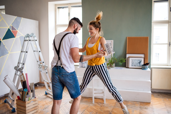 Mid adults couple having fun when painting wall indoors at home, relocation and diy concept.