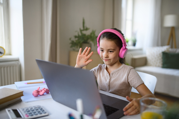 Schoolgirl having online lesson indoors at home, greeting teacher and coronavirus concept.