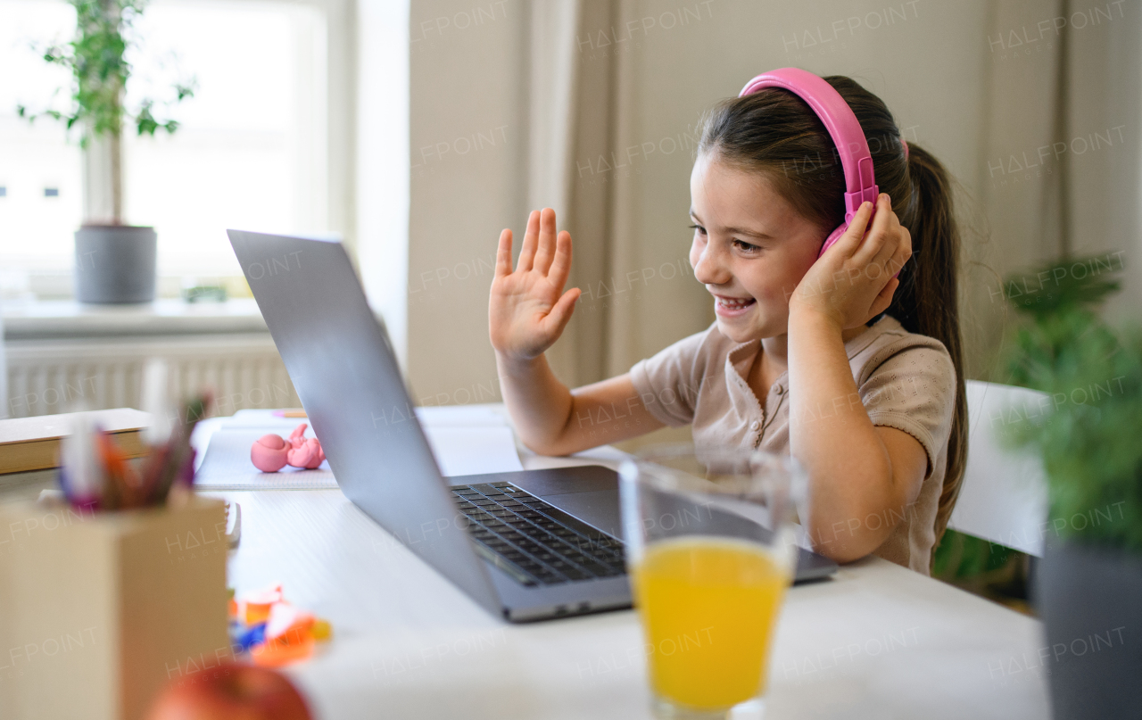 Schoolgirl having online lesson indoors at home, greeting teacher and coronavirus concept.