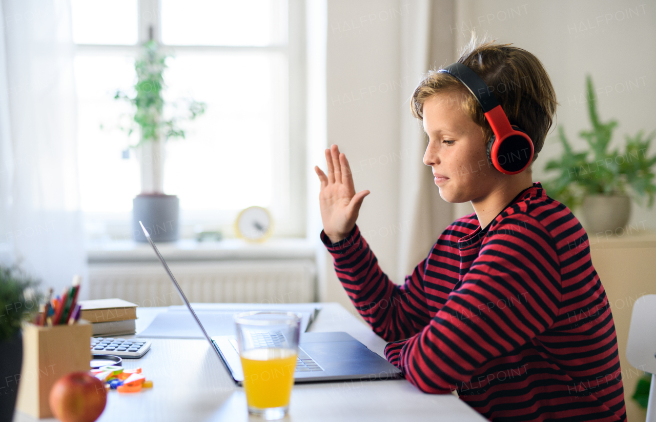 Schoolboy having online lesoon indoors at home, greeting teacher and coronavirus concept.