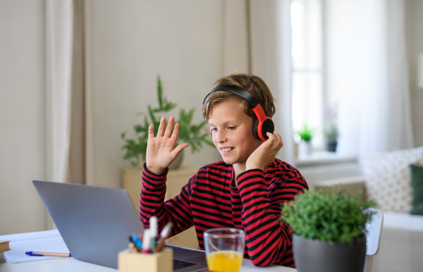 Schoolboy having online lesoon indoors at home, greeting teacher and coronavirus concept.