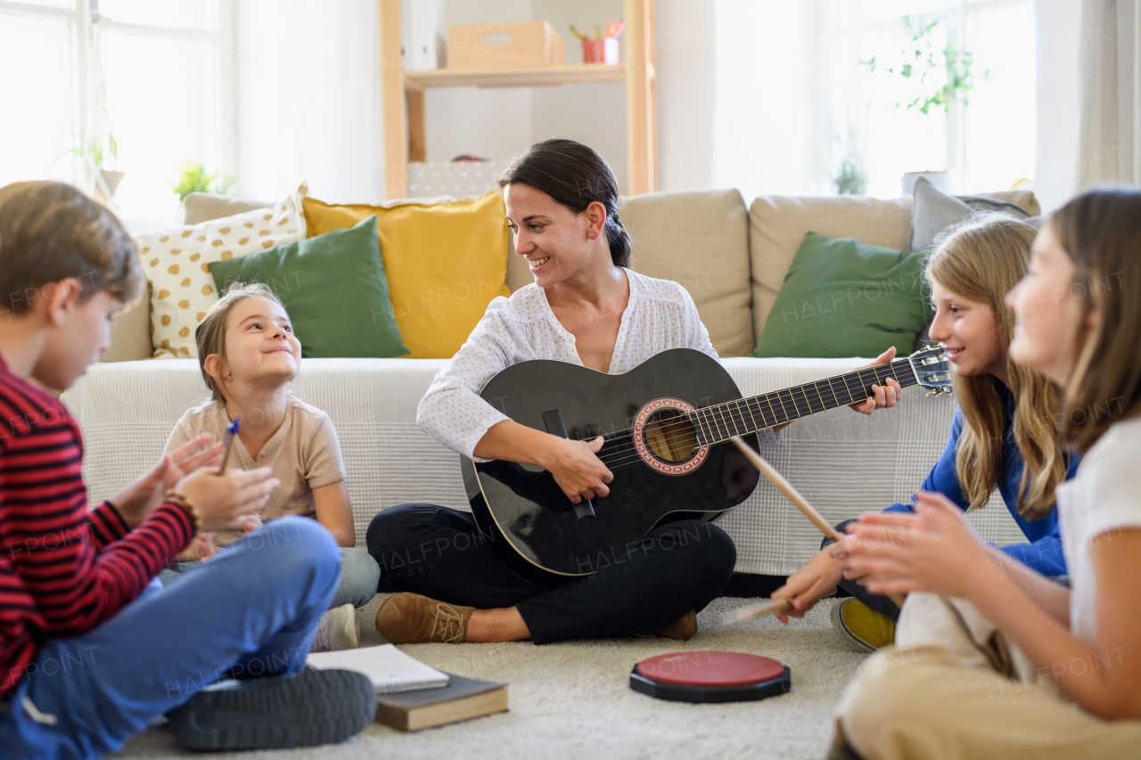 Group of cheerful homeschooling children with teacher having music lesson indoors, coronavirus concept.