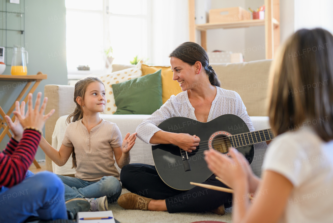 Group of cheerful homeschooling children with teacher having music lesson indoors, coronavirus concept.