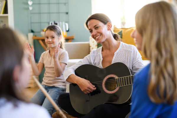 Group of cheerful homeschooling children with teacher having music lesson indoors, coronavirus concept.