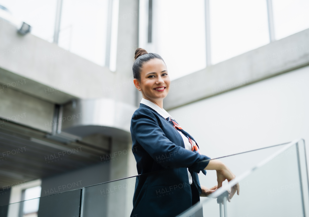 Front view portrait of attractive flight attendant standing on airport, looking at camera.