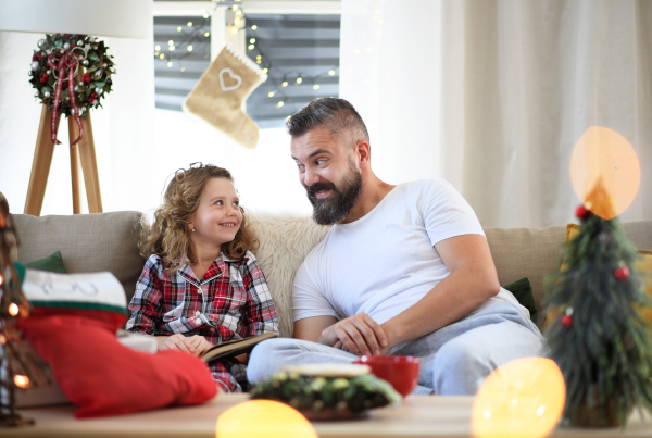 Portrait of father with small daughter indoors at home at Christmas, reading book.