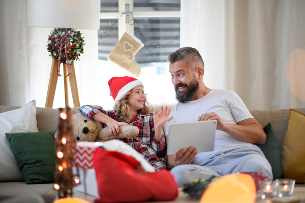 Portrait of father with small daughter indoors at home at Christmas, using tablet.