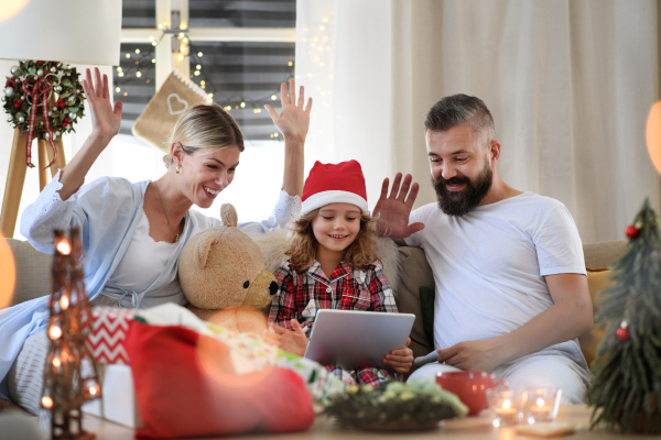 Family with small daughter indoors at home at Christmas, having video call on tablet.