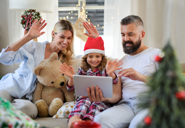 Family with small daughter indoors at home at Christmas, having video call on tablet.