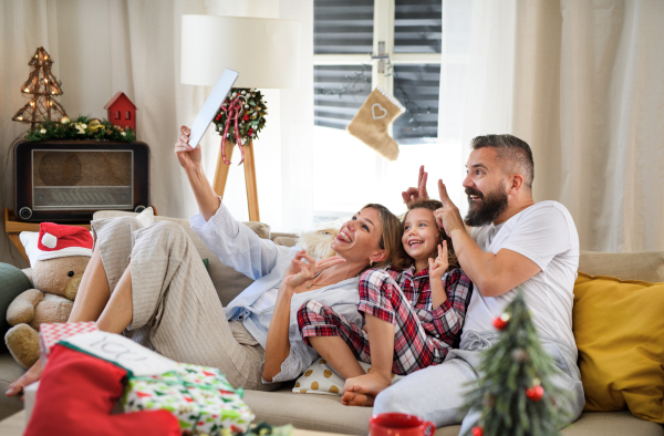 Family with small daughter indoors at home at Christmas, having video call on tablet.