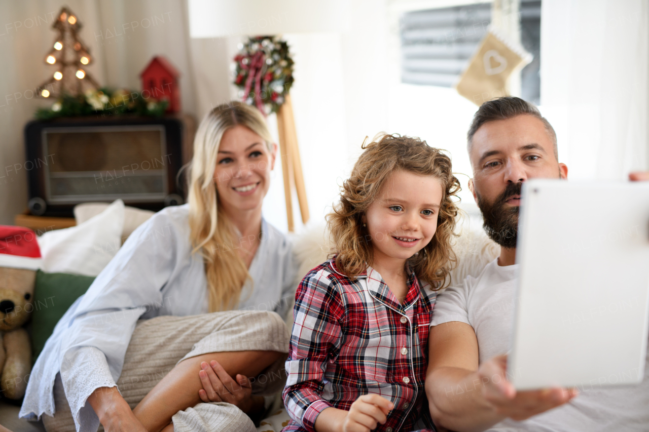 Family with small daughter indoors at home at Christmas, having video call on tablet.