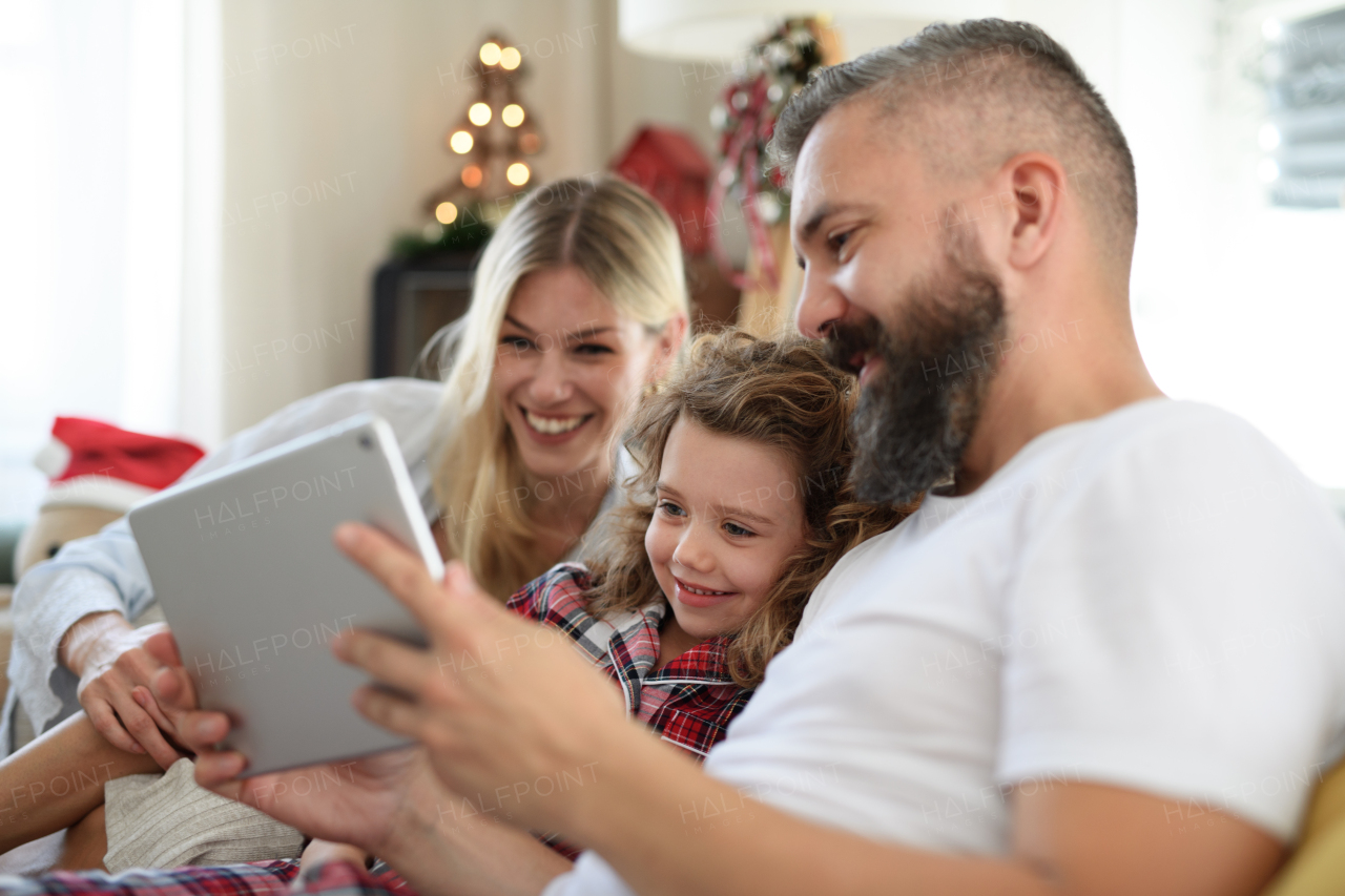 Family with small daughter indoors at home at Christmas, having video call on tablet.