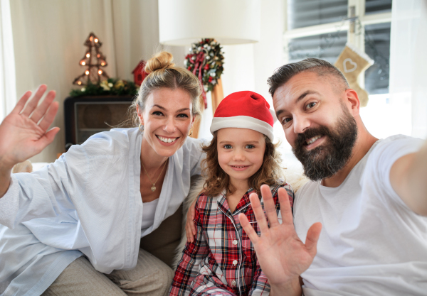 Front view of family with small daughter indoors at home at Christmas, taking selfie.