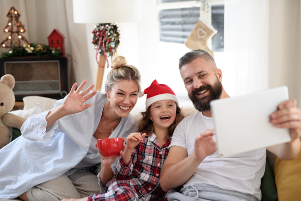 Family with small daughter indoors at home at Christmas, having video call on tablet.