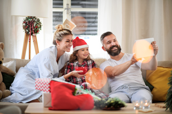 Family with small daughter indoors at home at Christmas, taking selfie with tablet.