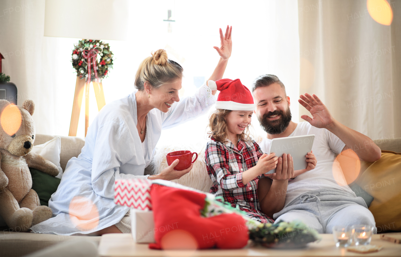 Family with small daughter indoors at home at Christmas, having video call on tablet.