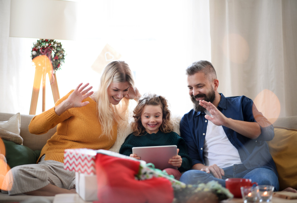 Family with small daughter indoors at home at Christmas, having video call on tablet.