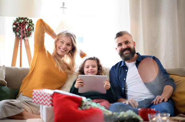 Couple with small daughter indoors at home at Christmas, having video call on tablet.