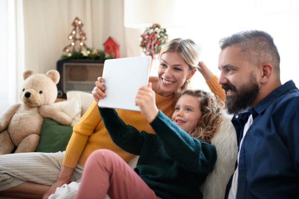 Family with small daughter indoors at home at Christmas, having video call on tablet.