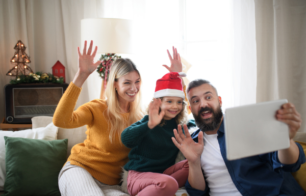 Family with small daughter indoors at home at Christmas, having video call on tablet.