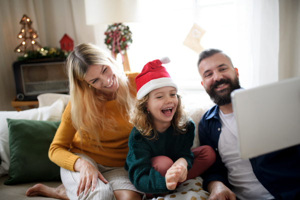 Family with small daughter indoors at home at Christmas, having video call on tablet.