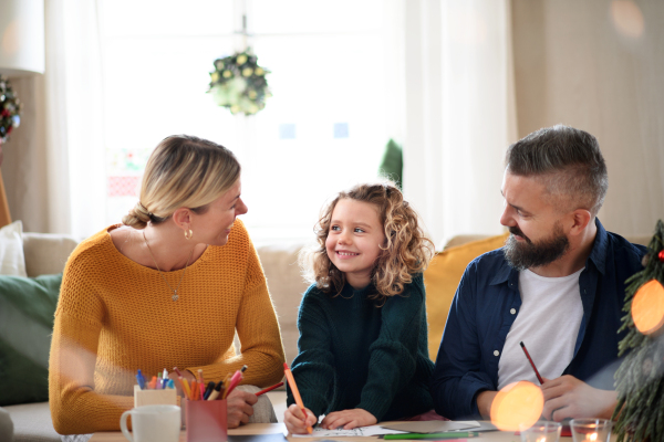 Happy family with small daughter indoors at home at Christmas, making Christmas cards.