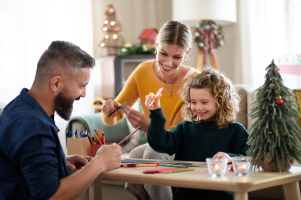 Happy family with small daughter indoors at home at Christmas, making Christmas cards.