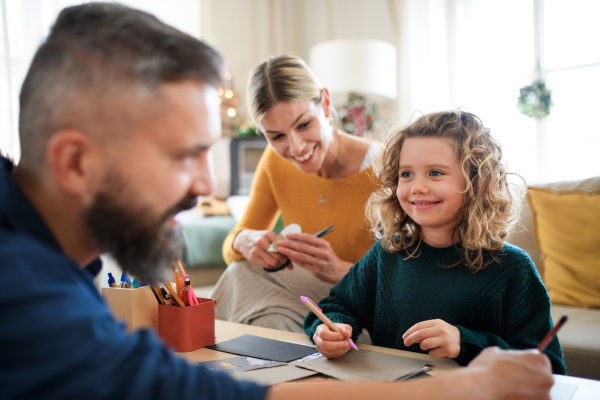 Happy family with small daughter indoors at home at Christmas, making Christmas cards.