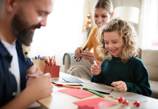 Happy family with small daughter indoors at home at Christmas, making Christmas cards.