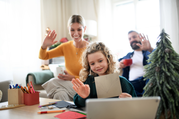 Family with small daughter indoors at home at Christmas, having video call on tablet.