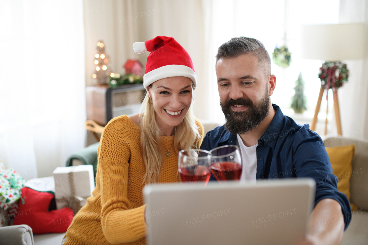 Front view of happy couple with wine indoors at home at Christmas, having video call with family or friends.